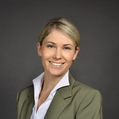 Eine lächelnde Frau in einem Anzug präsentiert sich vor neutralem Hintergrund, was das Engagement im Fussball symbolisiert.