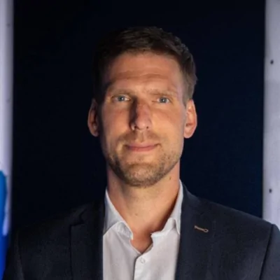 Ein selbstbewusster Mann in Anzug steht vor einer Bannerwand und repräsentiert die Initiative für Vielfalt im Fußball.