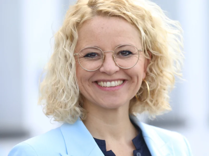 Jana Bernhard lächelt in einem blauen Blazer, symbolisiert die Vielfalt und Veränderung im Fußball.