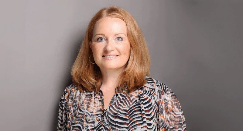 Claudia Wagner lächelt in einem eleganten Outfit vor einem neutralen Hintergrund und verkörpert die Vielfalt im Fußball.