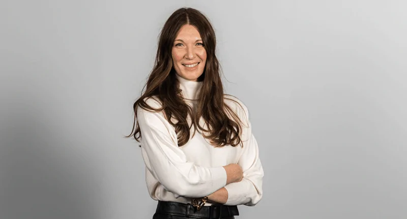 Sabrina Ratih steht mit einem Lächeln vor neutralem Hintergrund und repräsentiert die Vielfalt im Fußball.