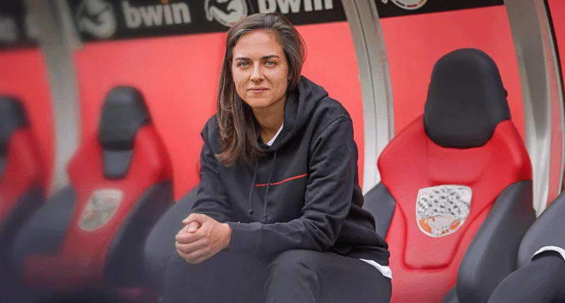 Sabrina Wittmann sitzt nachdenklich auf der Trainerbank und repräsentiert die Veränderung im Fußball.