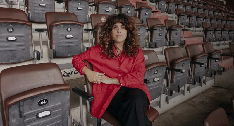 Stephanie Goncalves Norberto sitzt nachdenklich in einem leeren Stadion, das den Fußball und seine Vielfalt symbolisiert.